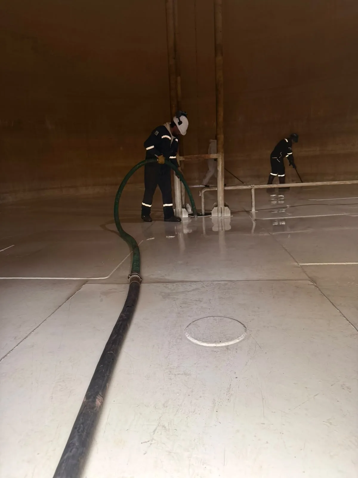 Trabajadores y mangueras en el interior de un gran recinto industrial.