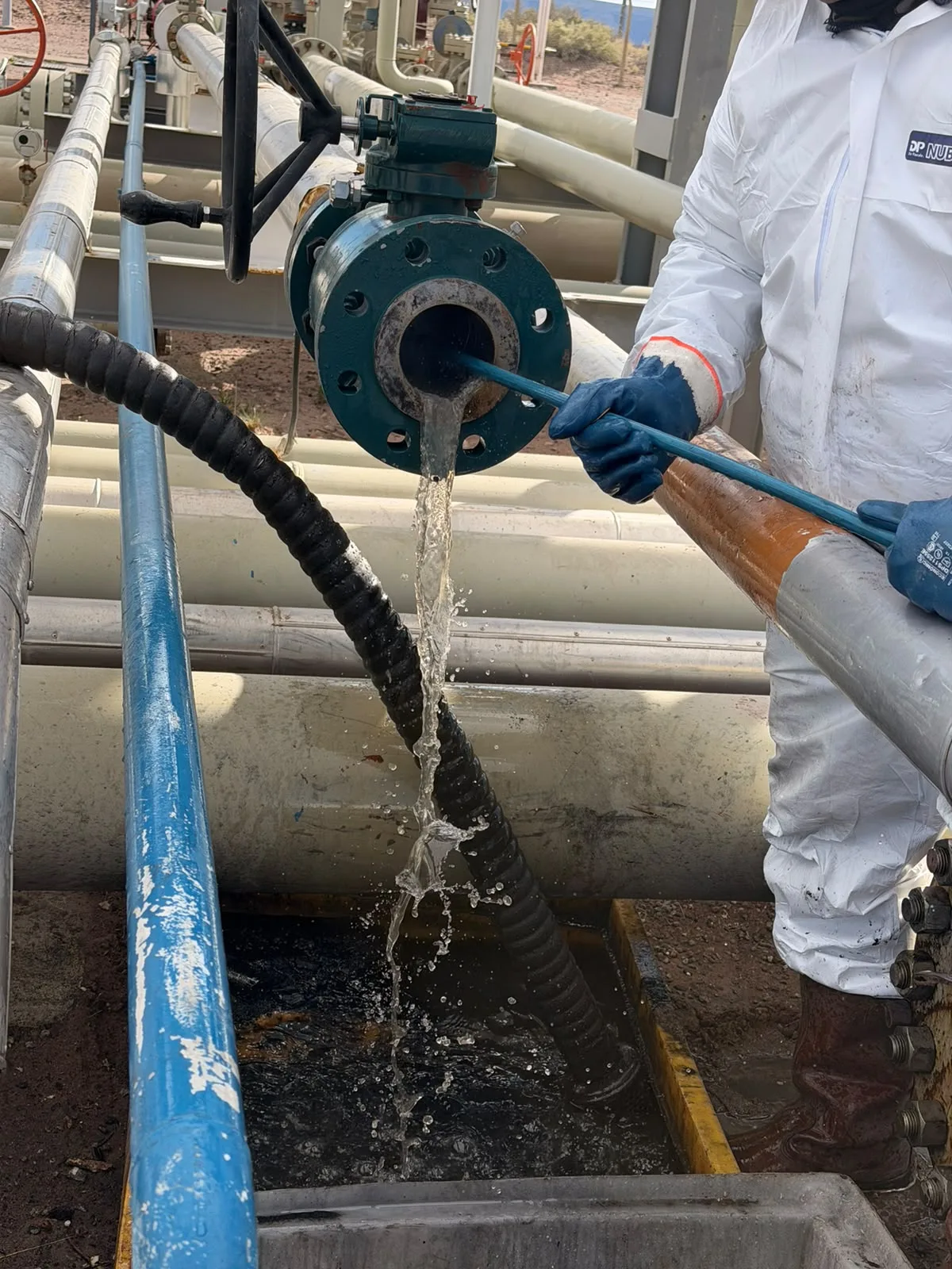Detalle de un trabajador con protección blanca, una manguera y una conexión industrial.